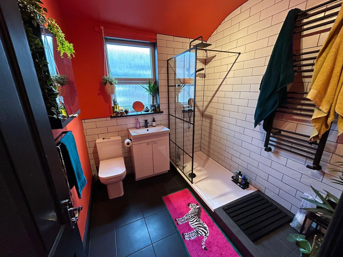 Bathroom with white metro tiling, black shower screen and bold red walls, tiled by English Rose